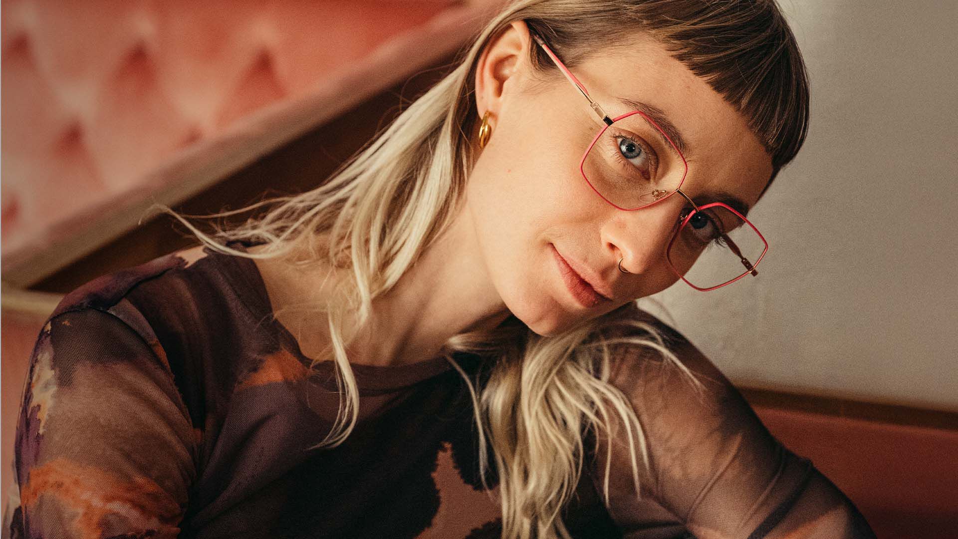 Nainen istuu sohvalla vaaleanpunaiset silm&auml;lasit kasvoilla